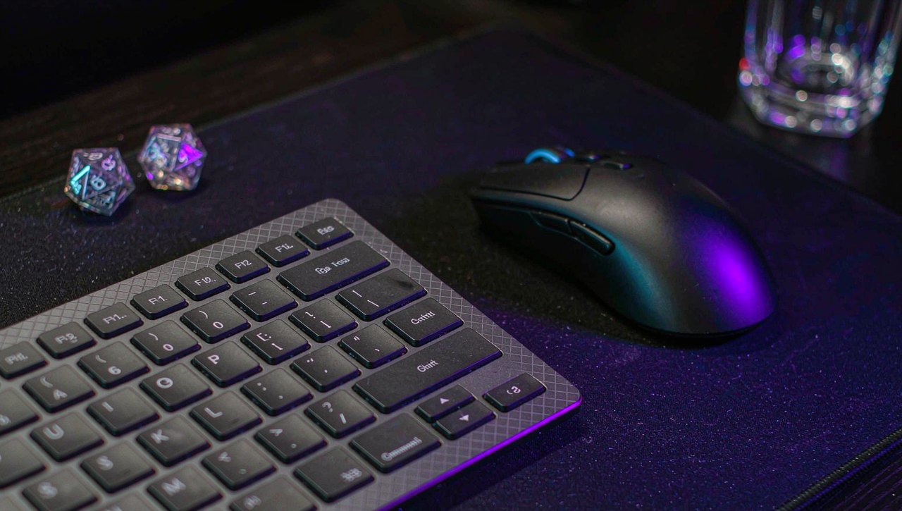 A mechanical keyboard and gaming mouse lit by purple and blue RGB light with two twenty-sided dice beside them on a dark desk