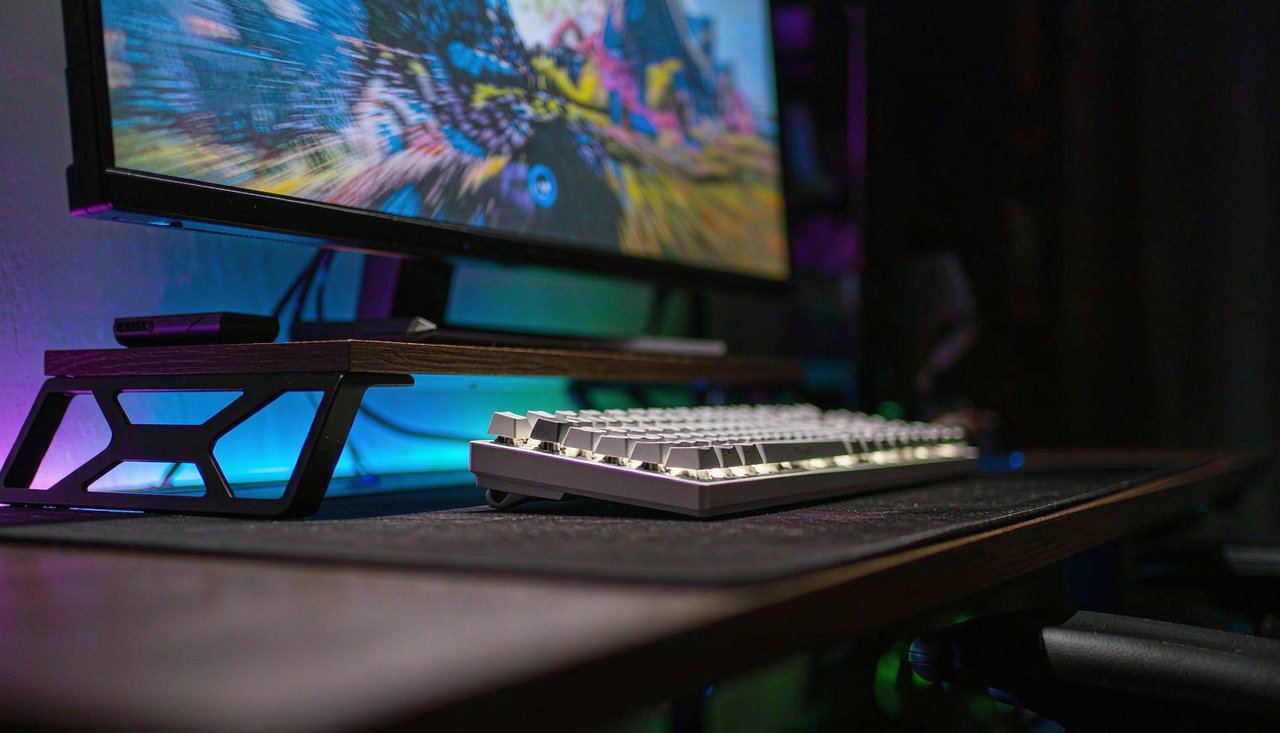 A gaming desktop setup at night with a mechanical keyboard and a monitor showing a motion-blurred racing game