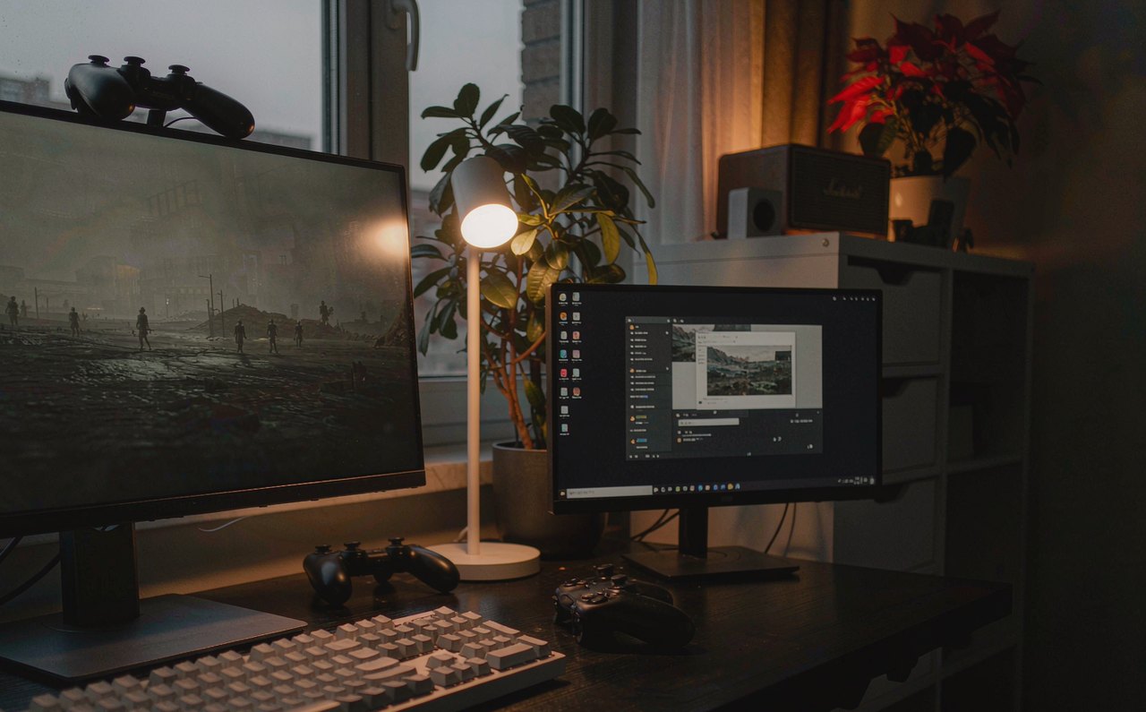 A widescreen gaming monitor on a desk displaying a dim, gray-toned landscape, with the Windows HDR settings screen visible on a second screen beside it