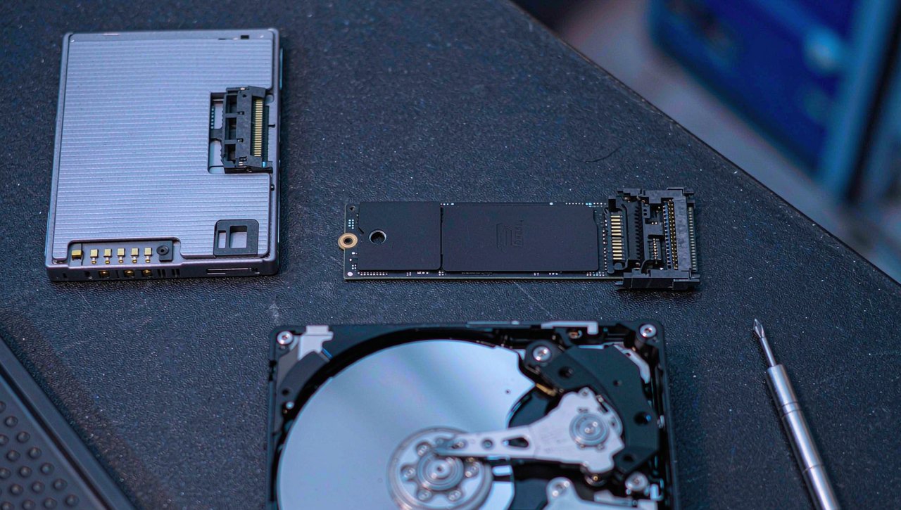 A 2.5-inch SSD, an M.2 stick, and an opened 3.5-inch mechanical hard drive laid out on an anti-static workbench mat